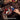 Hands assembling the SupreOwls Coffin of Roses building block set with red roses, skeleton ribs and blue butterflies on a dark tabletop.