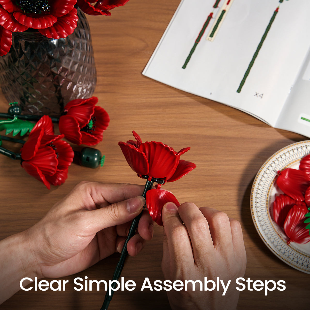 Red poppy flower bouquet building set assembly process showing hands attaching flower pieces with instruction guides and loose components on a table.