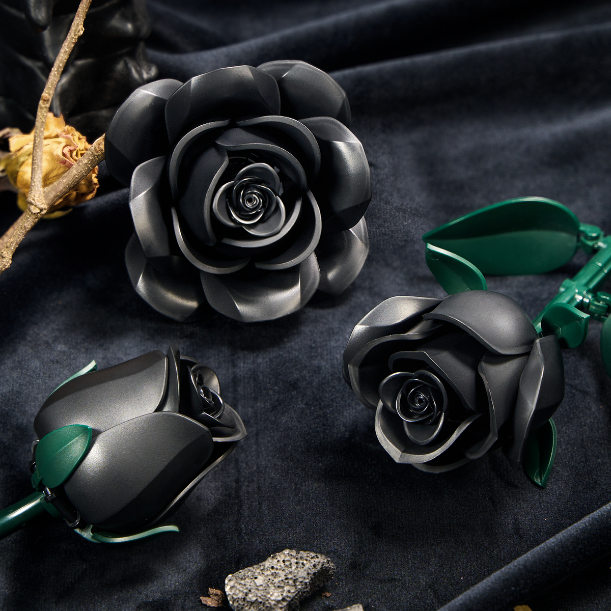 Close-up view of three black roses from a building block set, showing layered petals, detailed flower structures, and green leaves arranged on a dark fabric surface.
