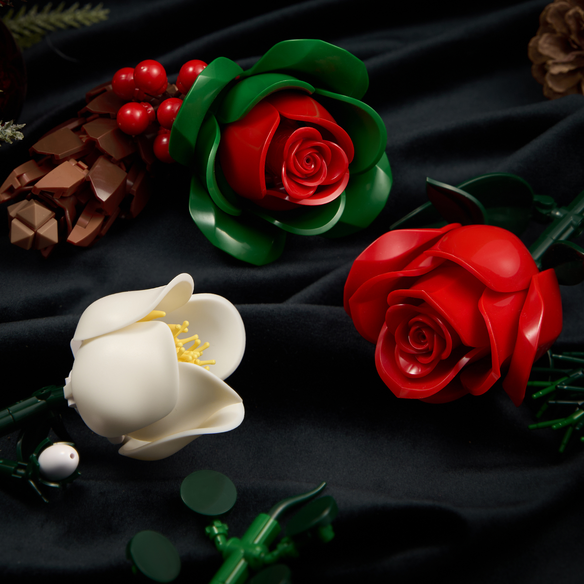 Christmas rose brick bouquet building block set detail view featuring red roses, a green rose bloom, white Christmas flowers, holly berries, pinecones, and green floral components arranged on a dark fabric background.