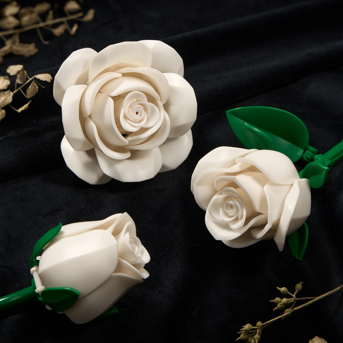 Close-up view of white rose building blocks featuring layered petals, realistic flower details, and green leaves arranged on a dark fabric background.