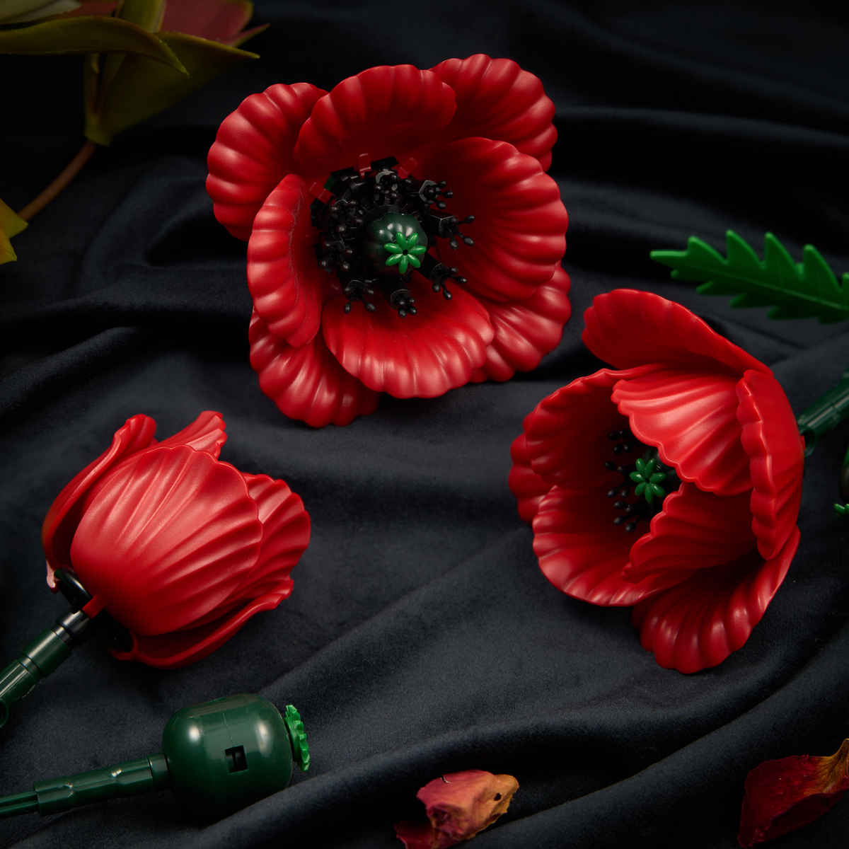 Close-up view of red poppy building blocks featuring detailed petals, black flower centers, and green leaves arranged on a dark surface.