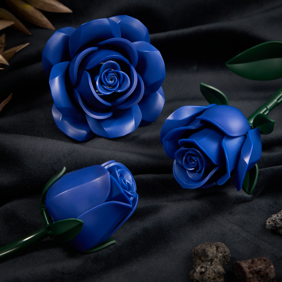 Close-up view of blue rose flowers with layered petals and green stems, arranged on a dark fabric surface to highlight their detailed structure and elegant floral design.