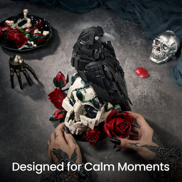 Hands assembling the Gothic Raven & Skull Art building set with a black raven, white skull and red roses on a dark table